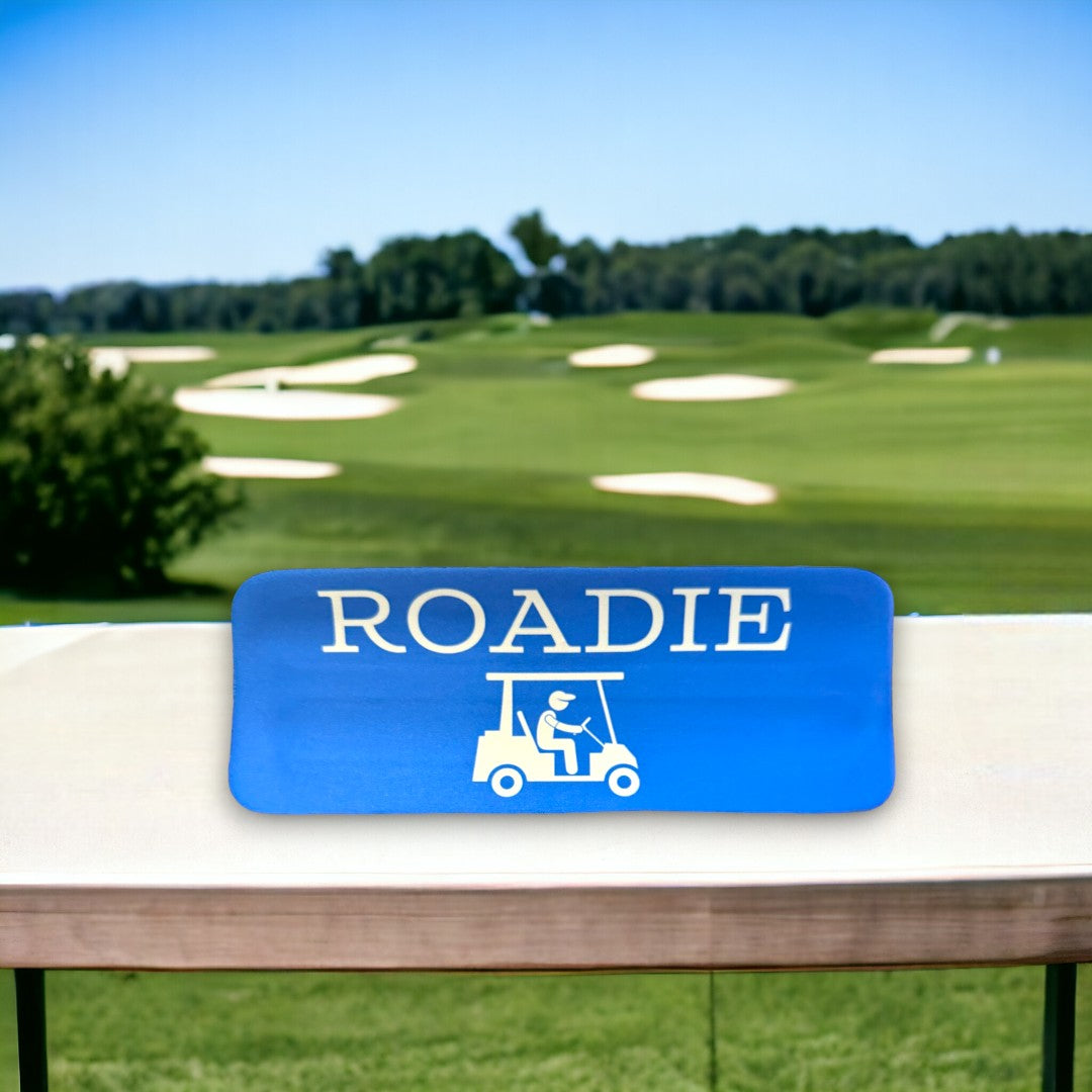 Blue custom drinkware sleeve branded with 'ROADIE' and a golf cart icon, displayed on a table with a golf course background, perfect as unique promo items.