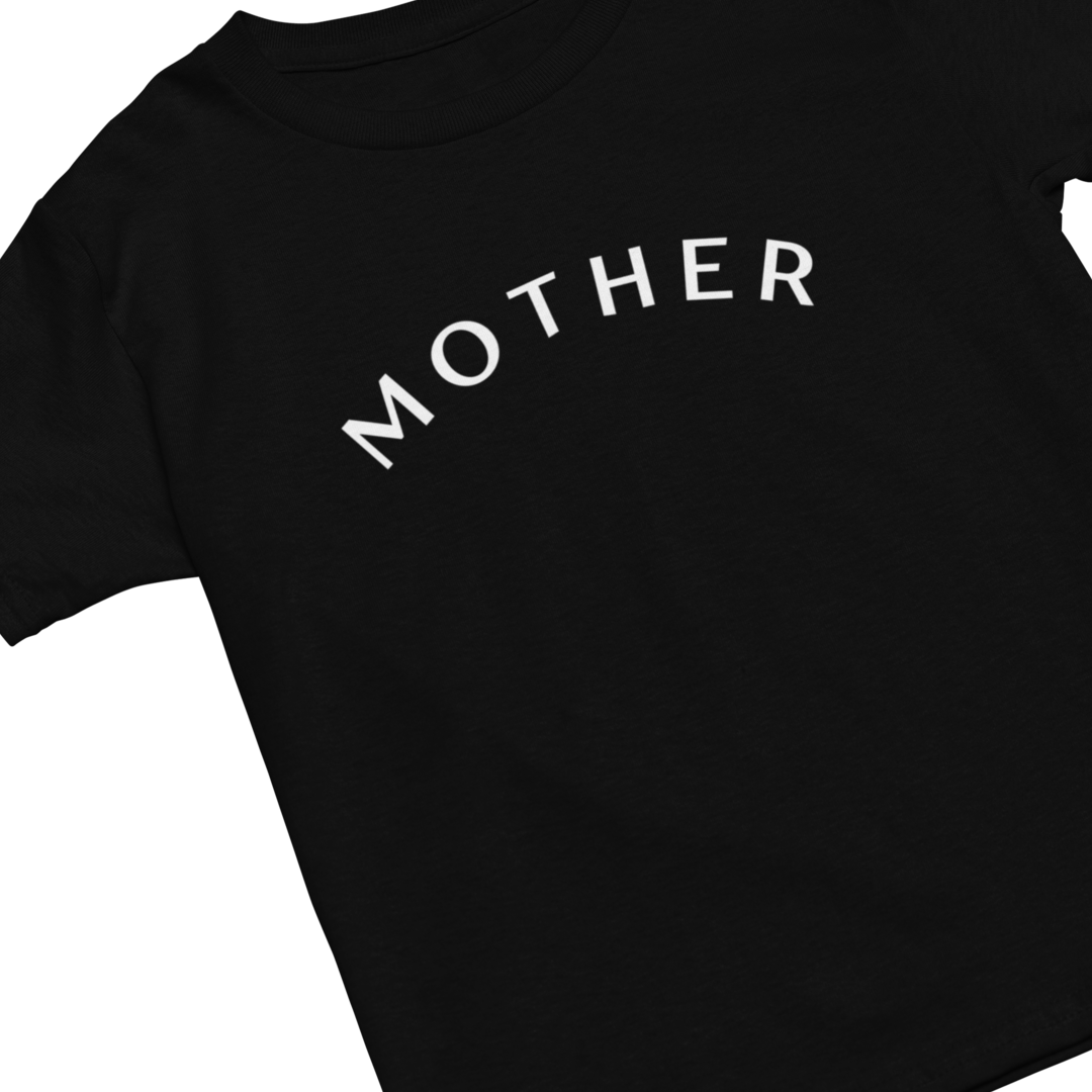 A chic and minimalist black t-shirt with the word "MOTHER" written in bold, white, capital letters. The text is slightly arched and centered across the chest area of this "Mother" Short Sleeve T-Shirt. The t-shirt is arranged diagonally in the image, with the neckline oriented toward the top left corner.