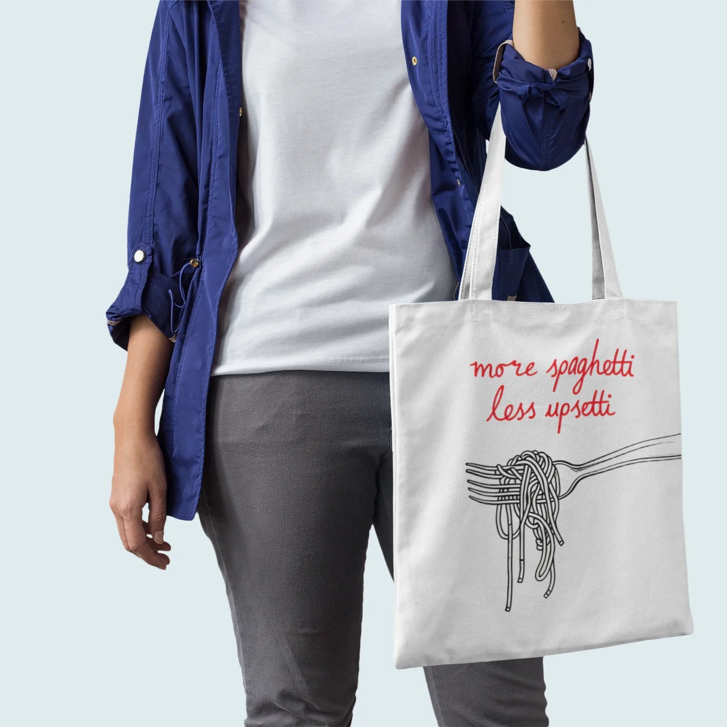 Person holding a tote bag with 'more spaghetti less upsetti' text and pasta illustration.