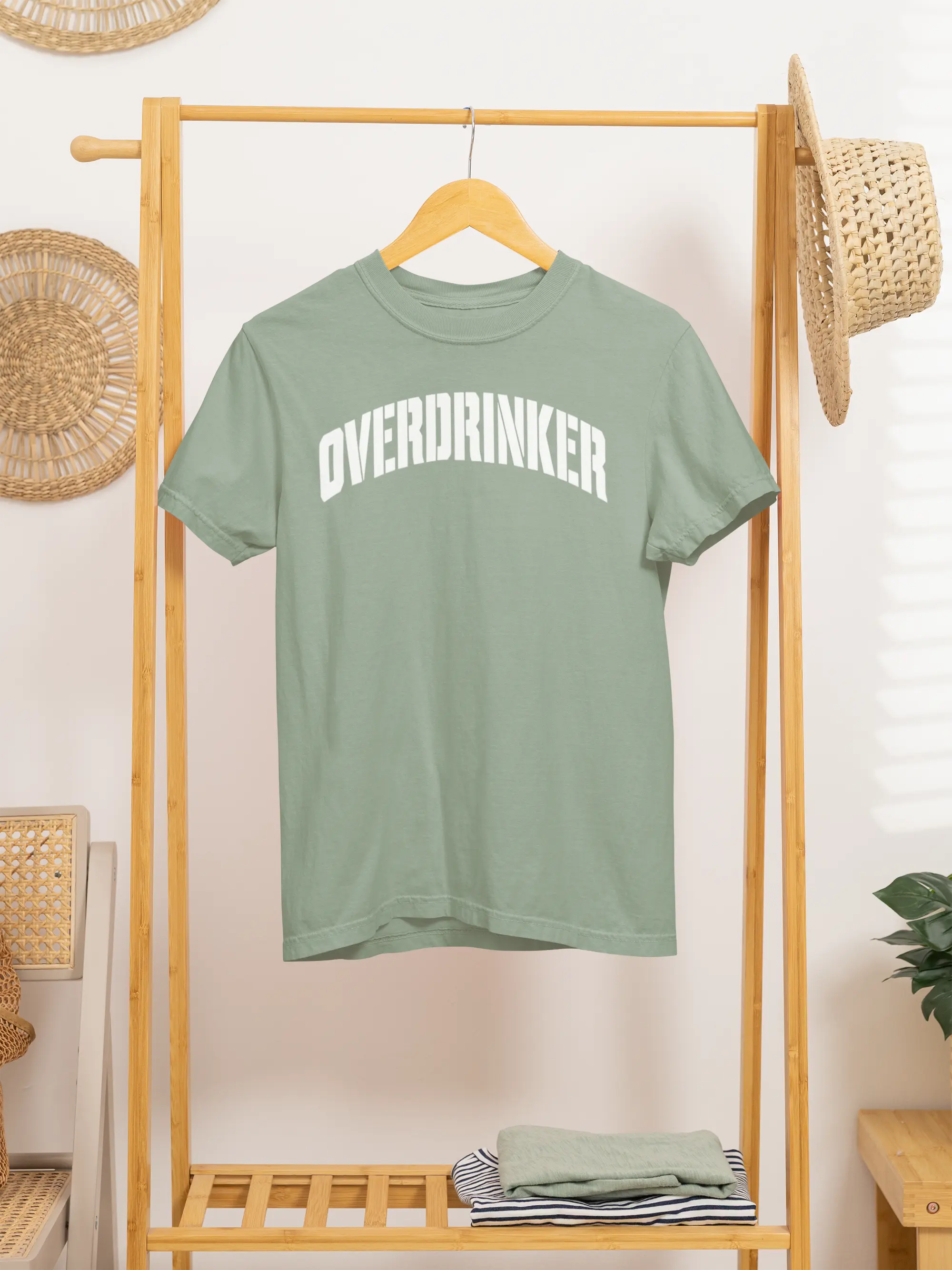 Green t-shirt with 'OVERDRINKER' text on a wooden rack.