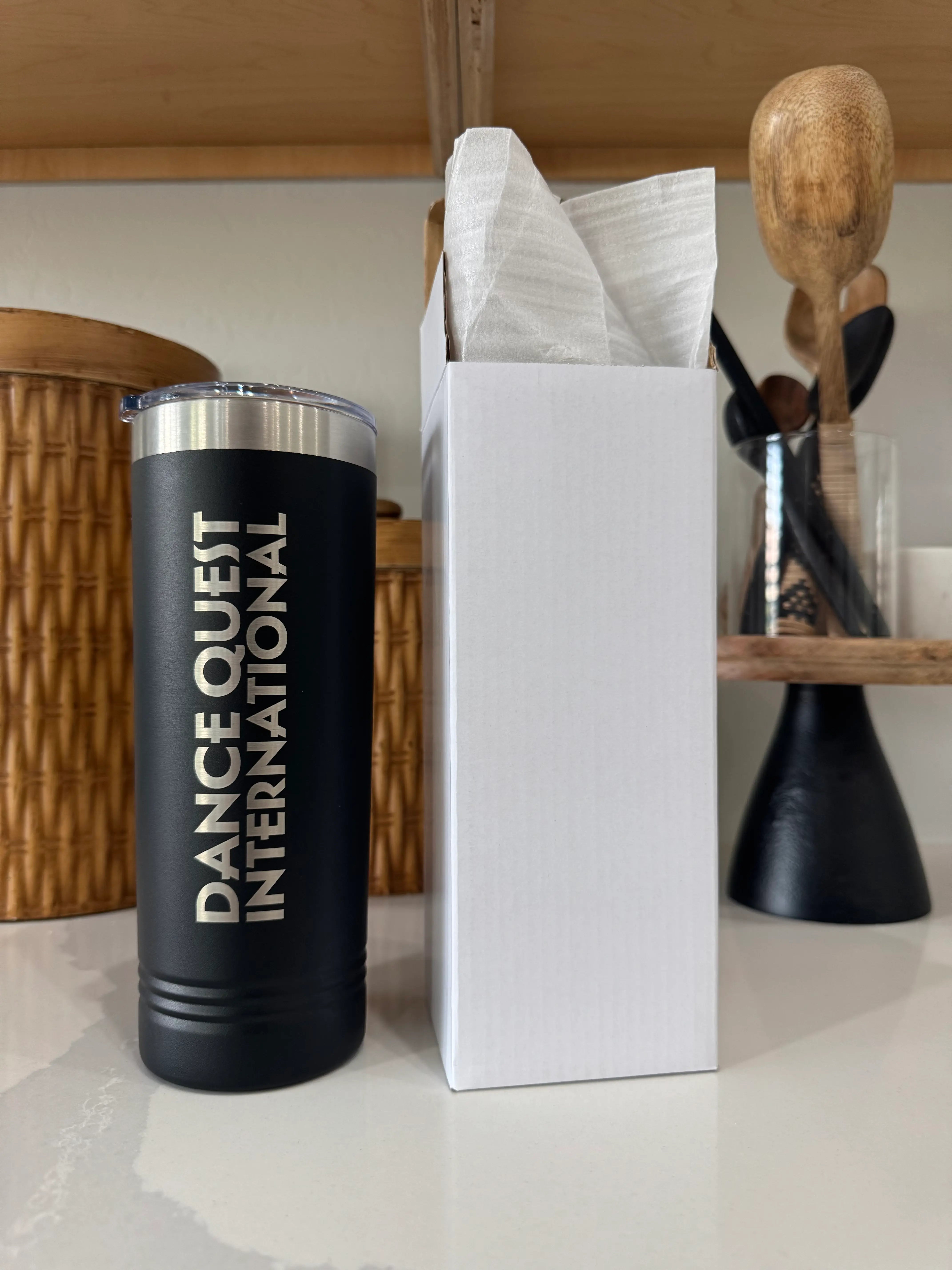 Customizable laser engraved tumbler in black with "Dance Quiet International" text next to white gift box - insulated stainless steel cup perfect for personalized business gifts and custom branding