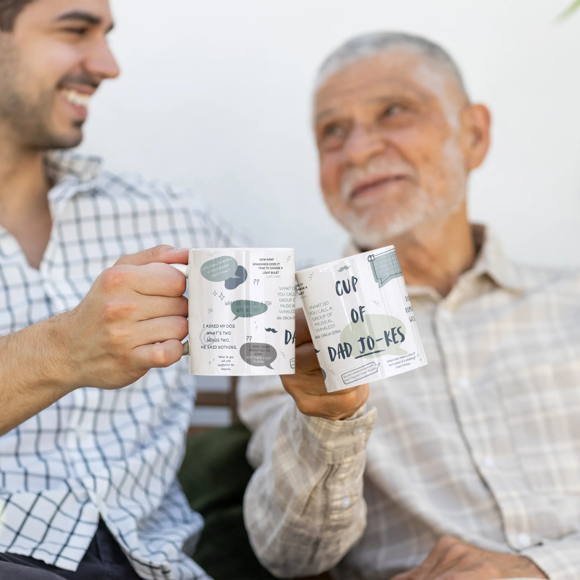 Two men holding mugs with text, sitting outdoors.