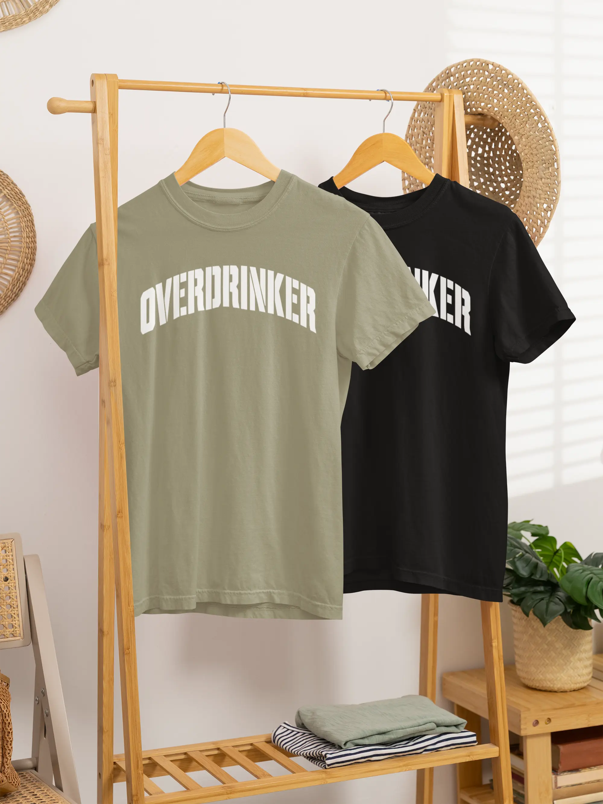 Two t-shirts, one green and one black, with 'OVERDRINKER' text on a wooden rack.