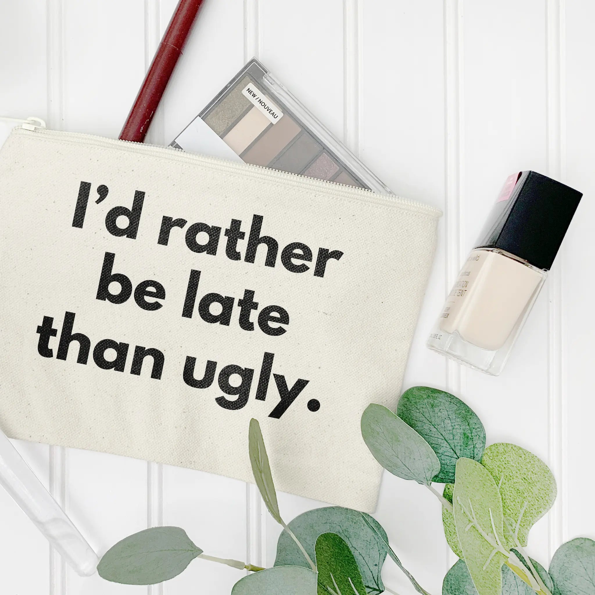 "I'd rather be late than ugly" makeup bag white canvas leaning against canisters lifestyle shot - funny cosmetic pouch for beauty enthusiasts