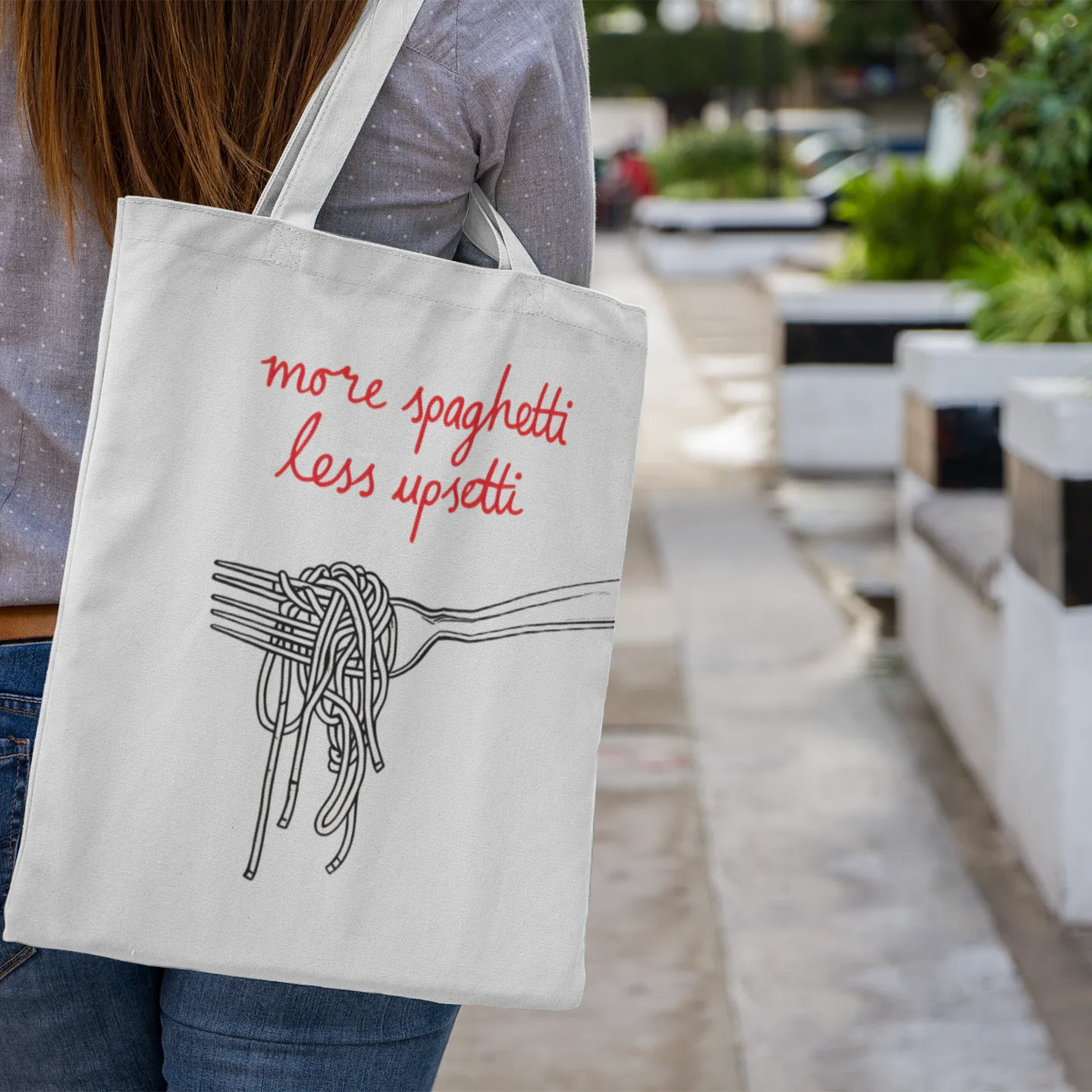 Person holding a tote bag with 'more spaghetti less upsetti' text and spaghetti illustration.