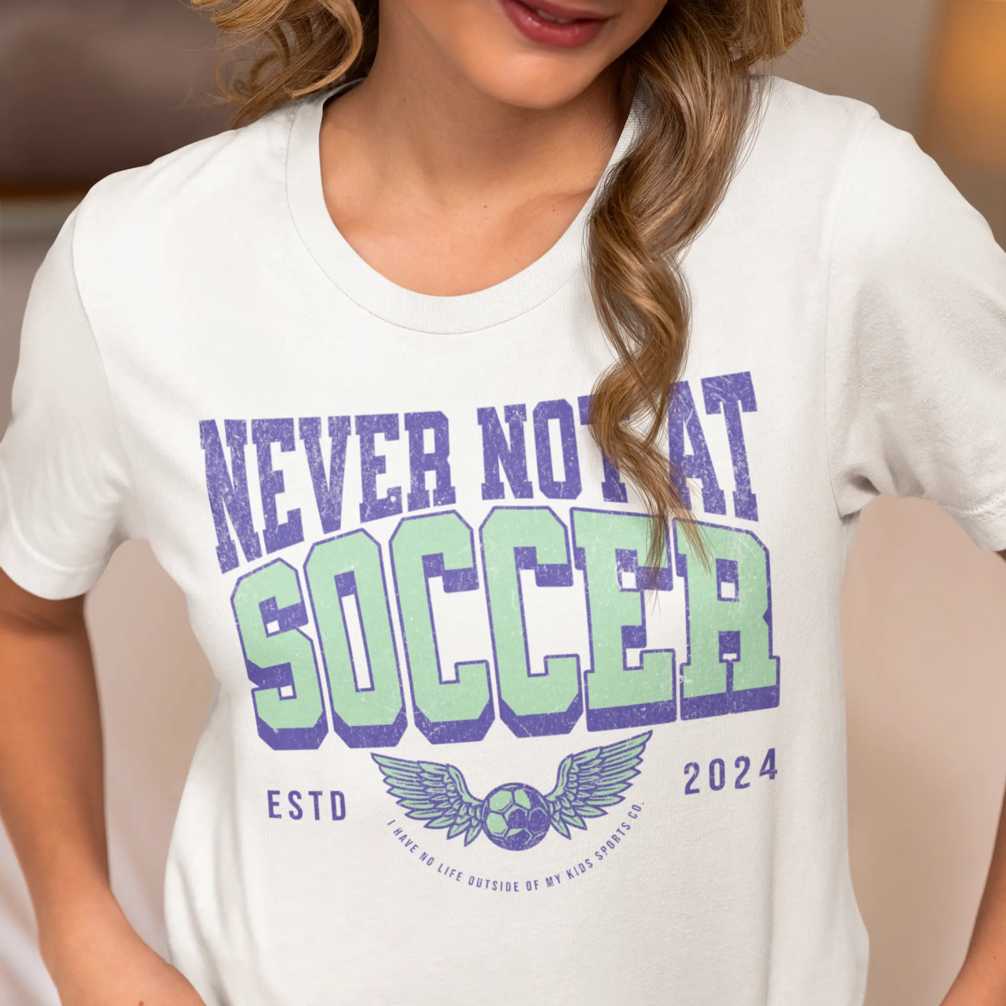 Front view "Never Not At Soccer" shirt with winged soccer ball design - soccer parent apparel for tournament life