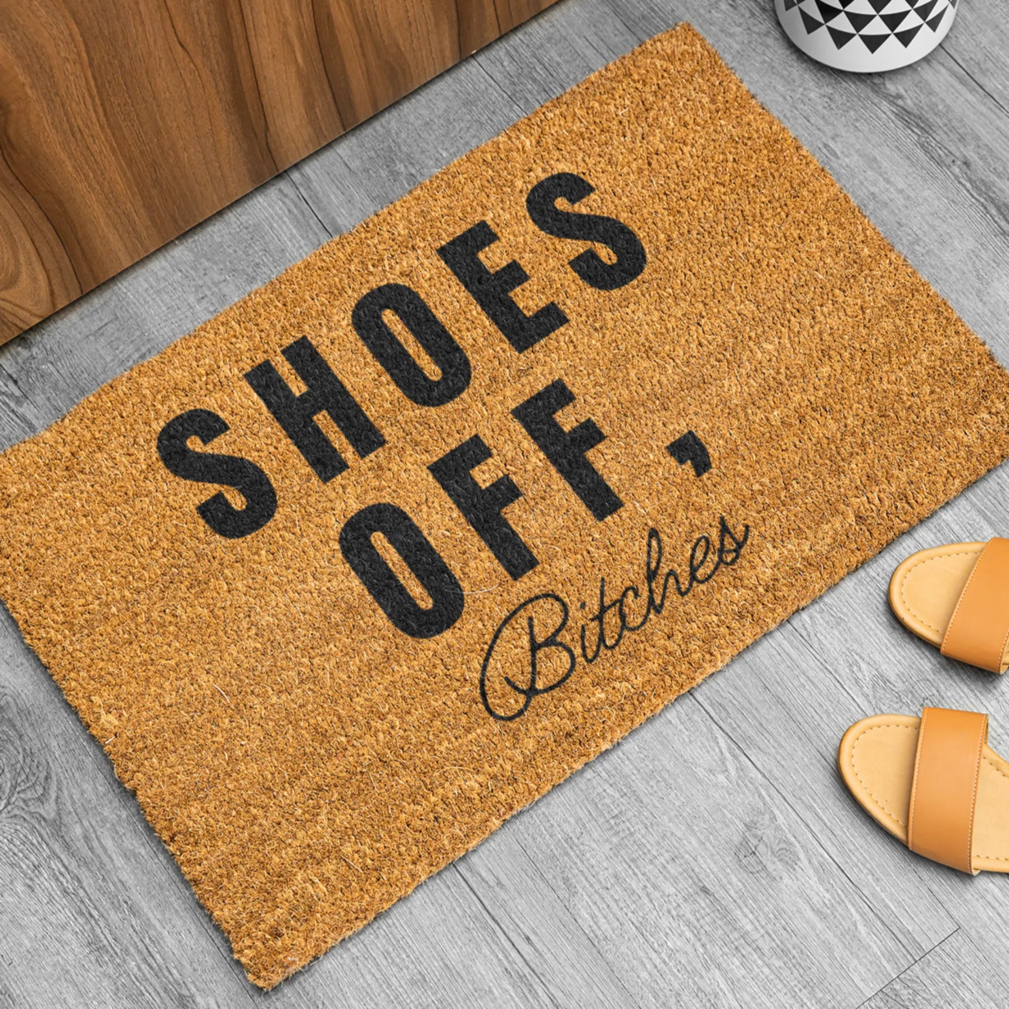 "SHOES OFF, Bitches" natural fiber doormat lifestyle shot - funny entrance mat with bold text and sandals for homes with attitude