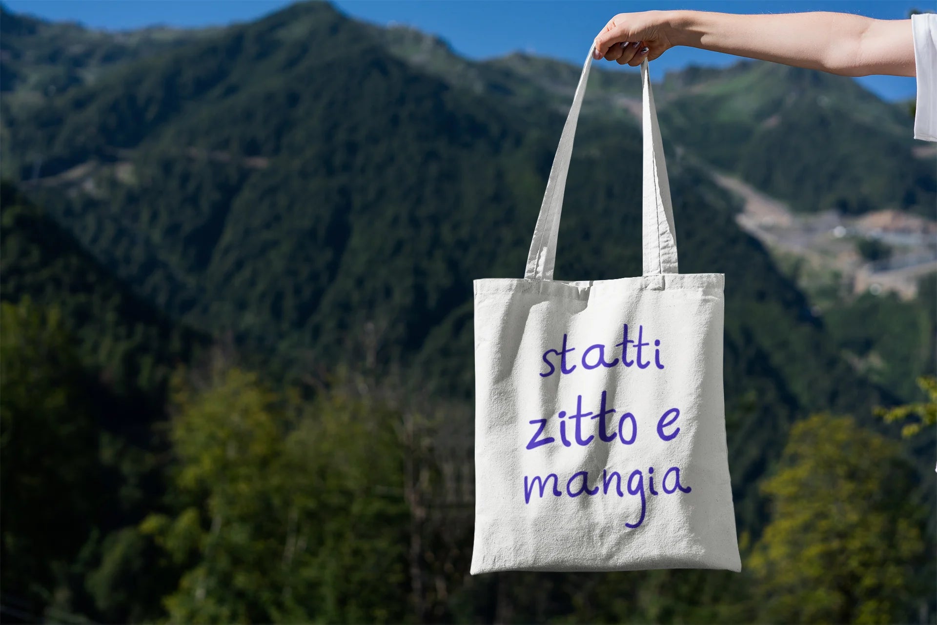 Tote bag with Italian text held against a mountainous landscape