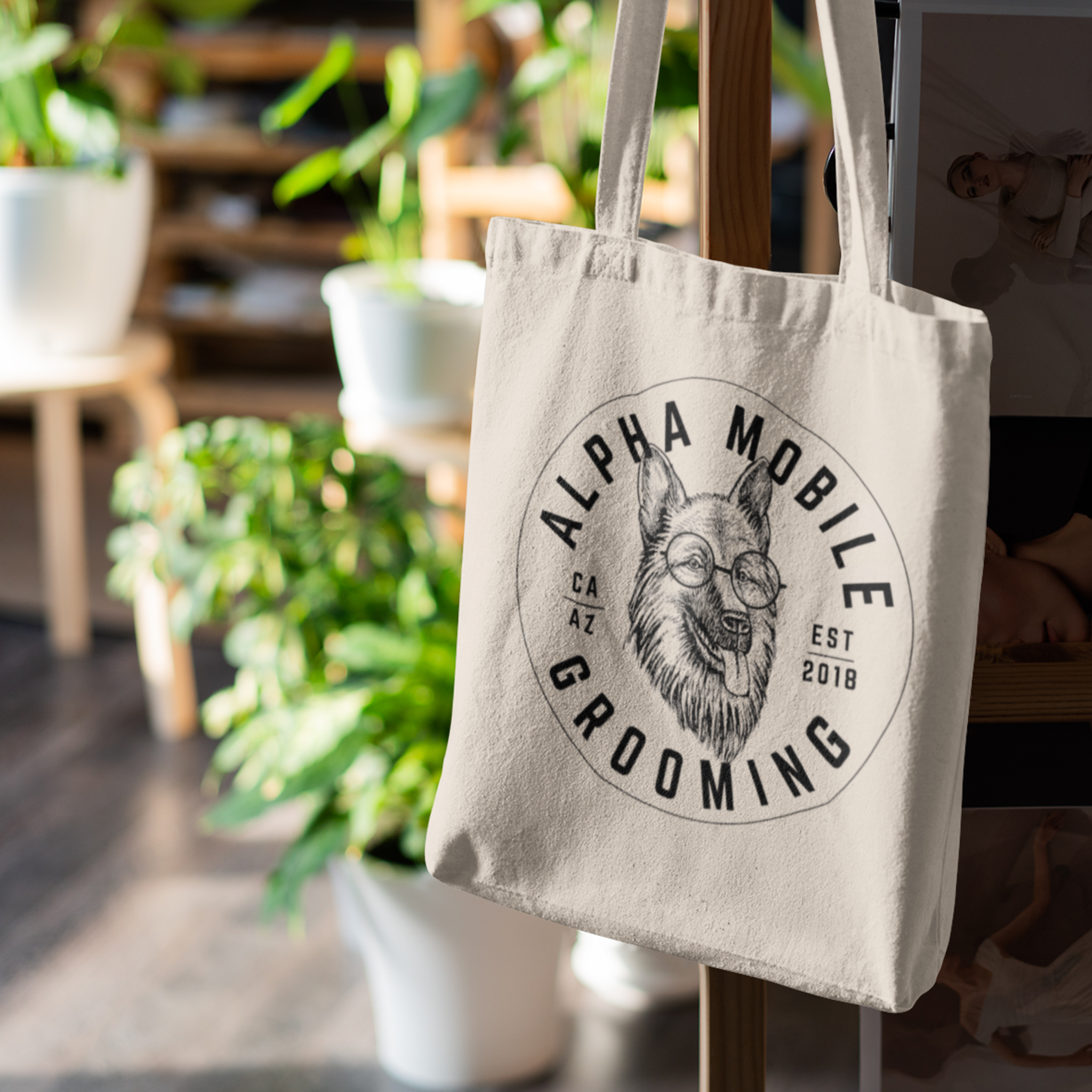 Canvas tote bag featuring Alpha Mobile Grooming logo, hanging in a green, plant-filled interior, ideal for eco-conscious pet owners.