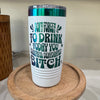 Image of a white insulated tumbler with green and black text that humorously reads, "Don't forget to drink today, you beautiful dehydrated bitch." The tumbler features a metallic green lid and sits on a wooden tray.