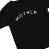 A chic and minimalist black t-shirt with the word "MOTHER" written in bold, white, capital letters. The text is slightly arched and centered across the chest area of this "Mother" Short Sleeve T-Shirt. The t-shirt is arranged diagonally in the image, with the neckline oriented toward the top left corner.
