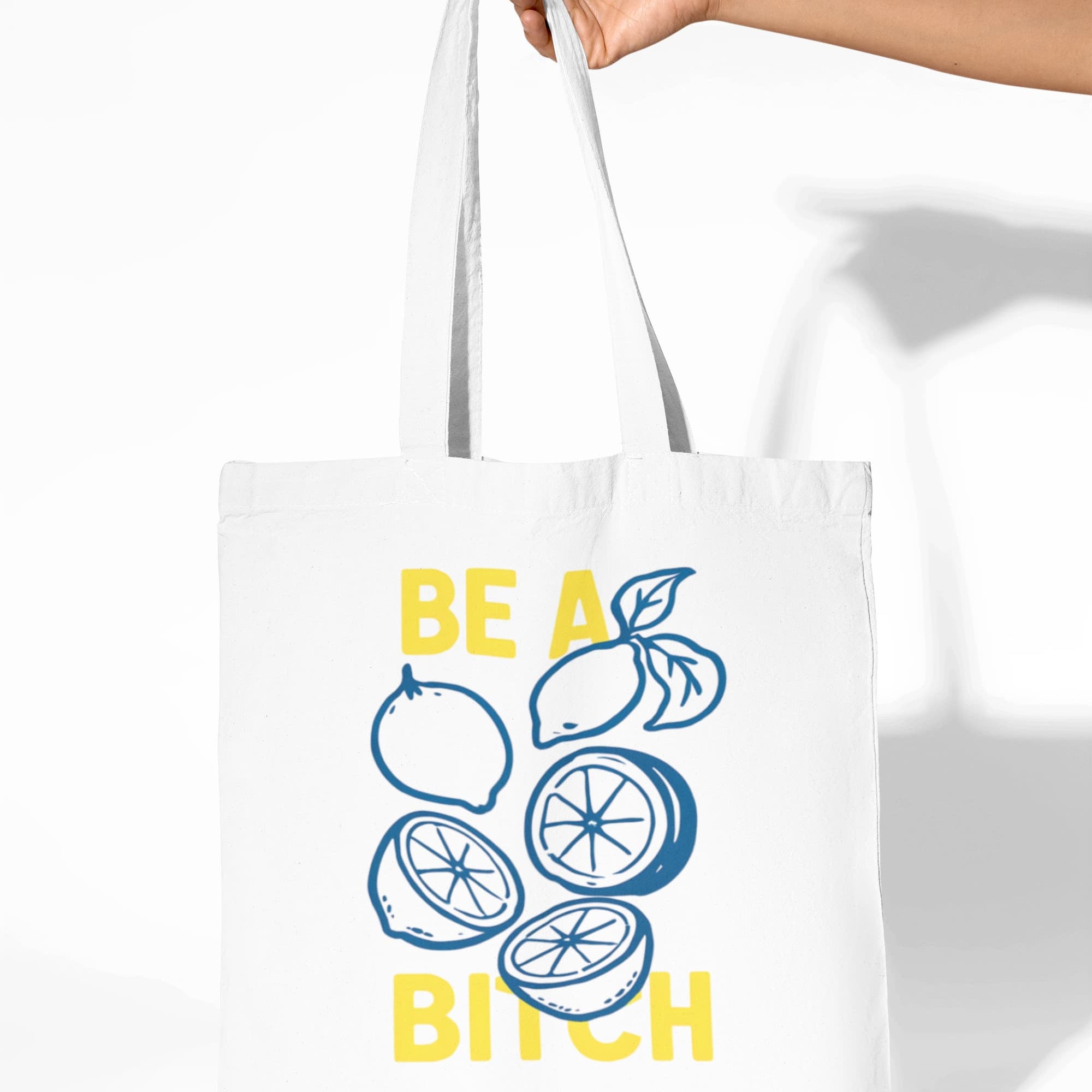 Tote bag with lemon design and text held by a hand on a white background