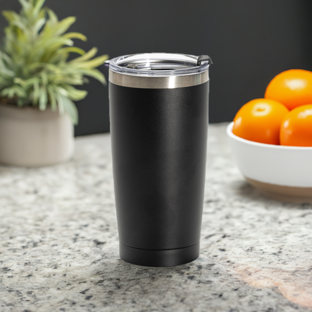 Black insulated tumbler on a kitchen counter, showcased next to a plant and oranges, perfect for personalized custom drinkware.