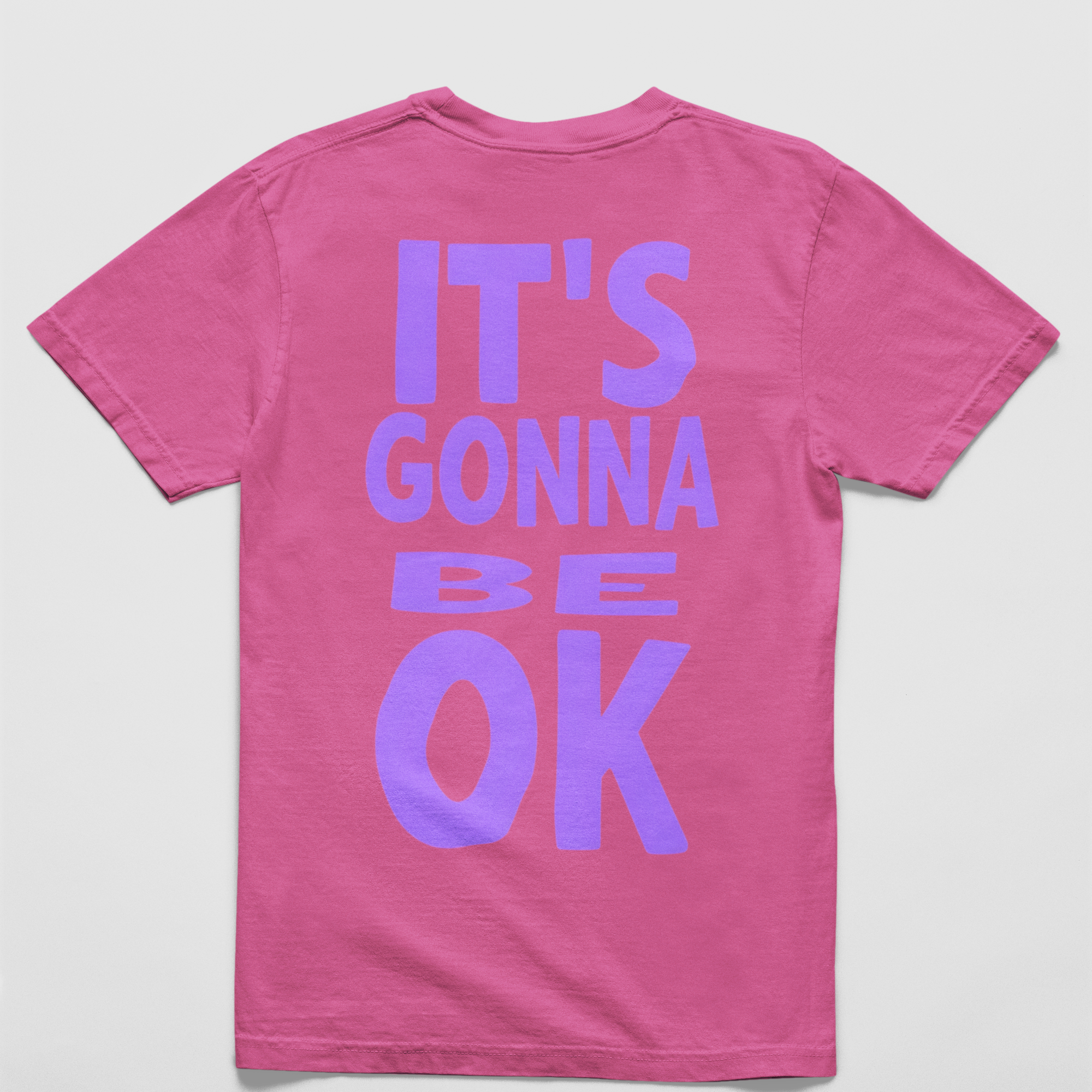 Oversized neon pink tee with "It’s Gonna Be OK" printed in bold purple text on the back, styled for casual and confident comfort.