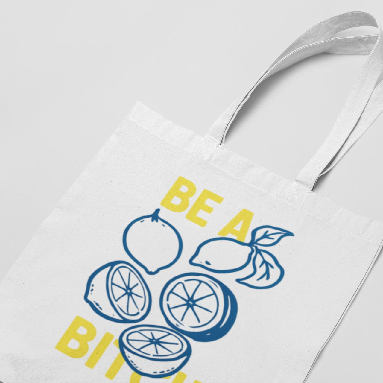 White tote bag with lemon design and text 'BE A LEMON BITCH' on a light gray background