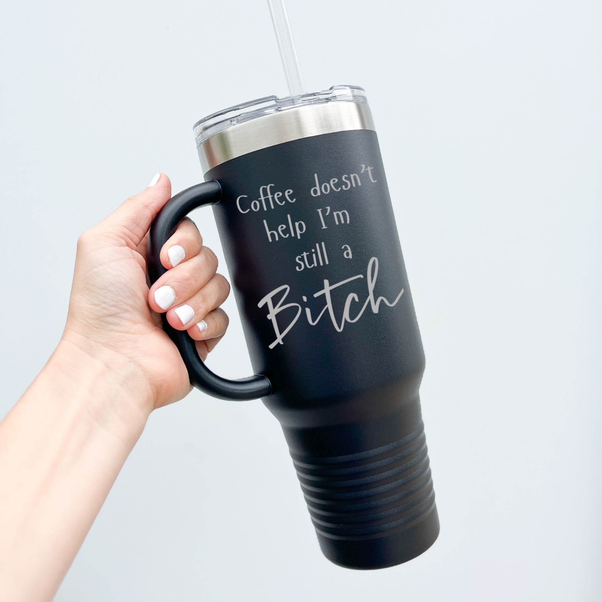Black insulated coffee tumbler with a humorous engraved quote, "Coffee doesn’t help, I’m still a bitch," held by a hand with white-painted nails against a plain background.