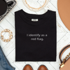 Folded black Comfort Colors t-shirt with “I identify as a red flag” design