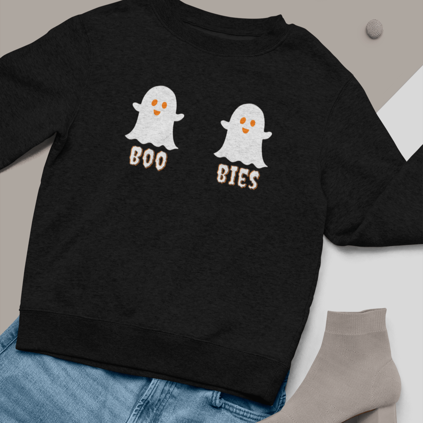 Black cozy Halloween sweatshirt featuring two cute ghost illustrations with the playful text "BOO BIES," styled with blue jeans and gray socks, perfect for casual festive wear.