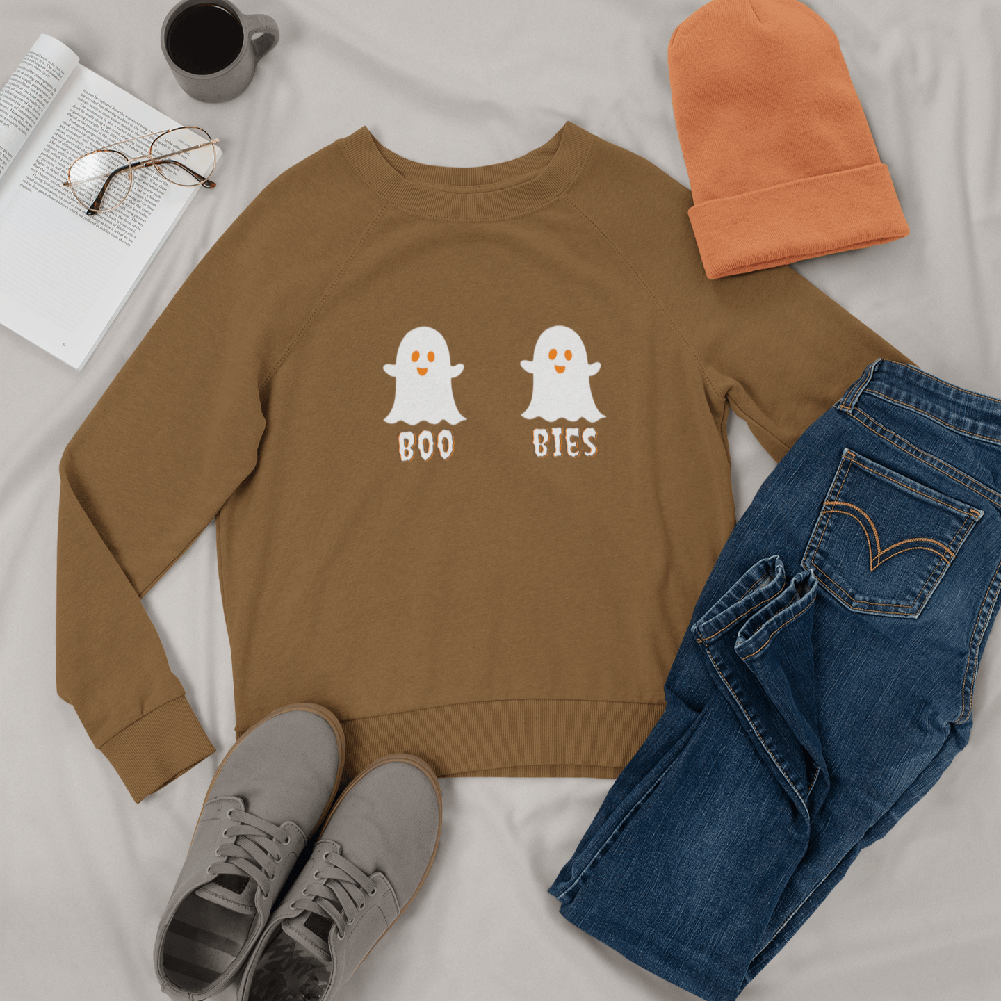 Brown cozy Halloween sweatshirt featuring two cute ghost illustrations with the playful text "BOO BIES," styled with jeans, gray sneakers, and a beanie, perfect for casual festive wear.