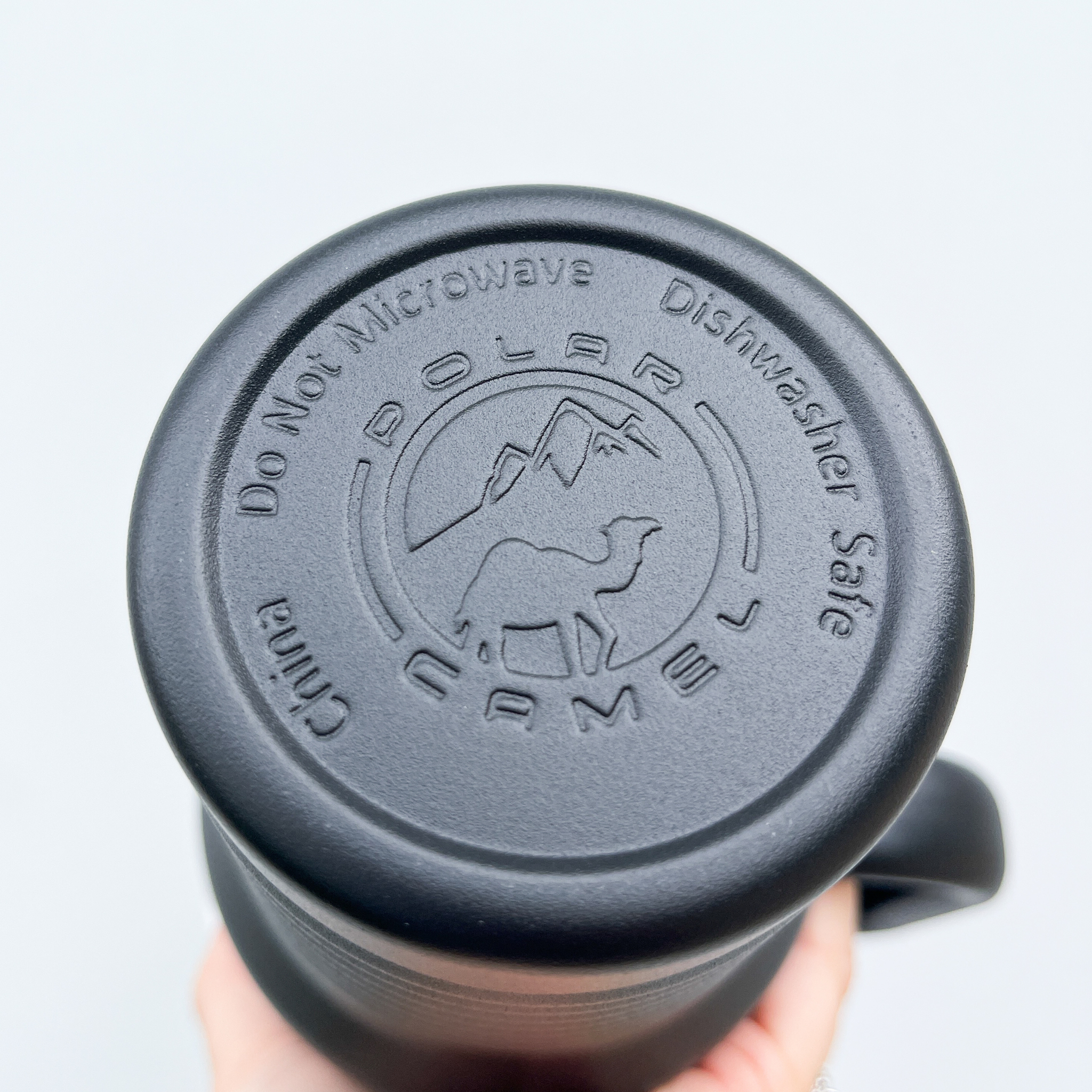 Close-up view of the bottom of a black tumbler featuring an embossed "Polar Camel" logo with a camel and mountains, along with the text "Do Not Microwave" and "Dishwasher Safe."