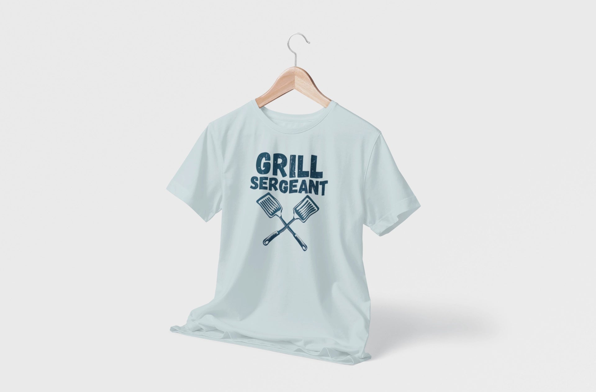 Light blue t-shirt with 'Grill Sergeant' text and crossed grill spatulas on a hanger against a white background
