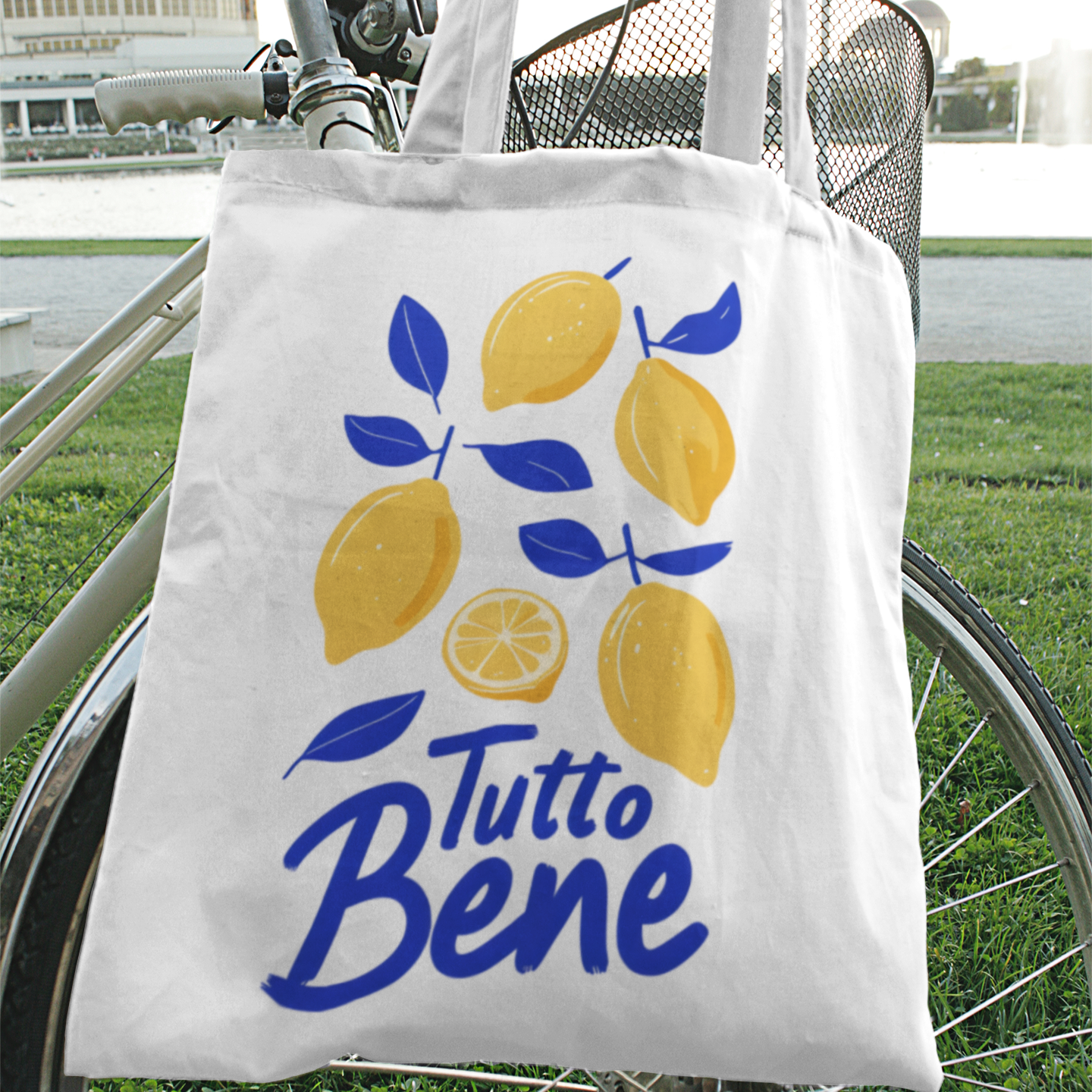 White cotton tote bag with yellow lemons and blue “Tutto Bene” text hanging from bike