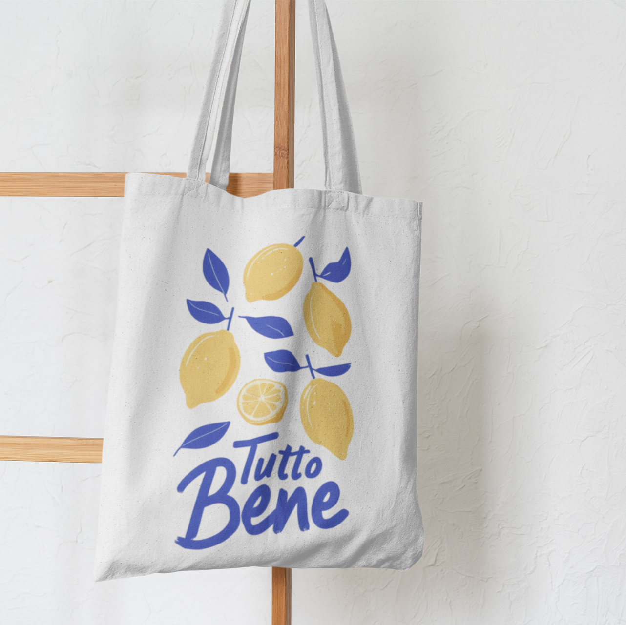 White cotton tote bag with yellow lemons and blue “Tutto Bene” text hanging from ladder