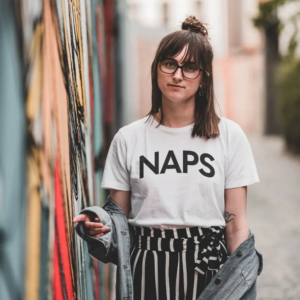 Person wearing a white t-shirt with 'NAPS' text, standing outdoors.