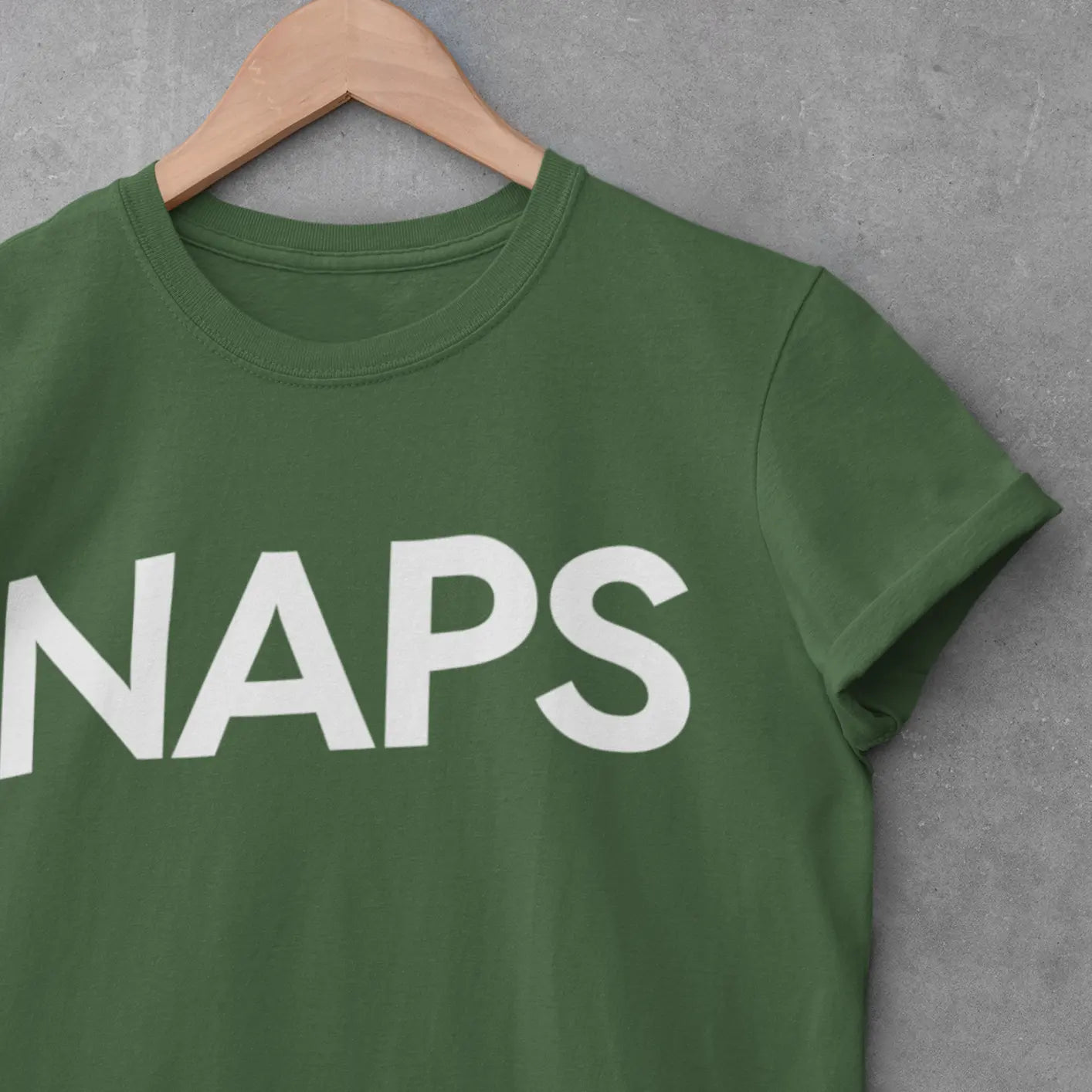 Close-up of crewneck t-shirt on hanger by a cement wall with bold “NAPS” text