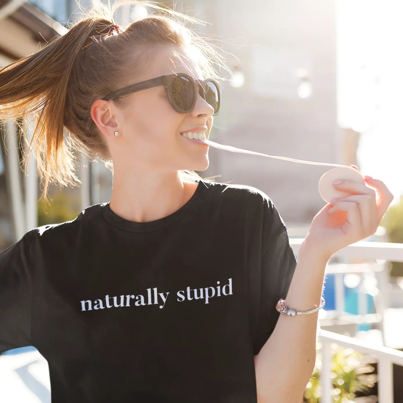 Casual women’s graphic tee that says “naturally stupid” worn outdoors in a scenic nature setting