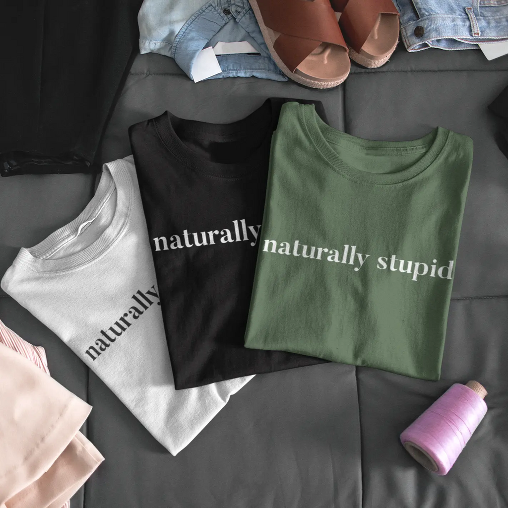 Women’s “naturally stupid” graphic t-shirt shown in an outdoor lifestyle mockup with nature background