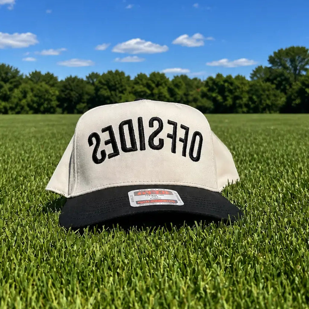 Two-tone trucker hat sitting on grass with embroidered “OFFSIDES” text, funny soccer hat for game day
