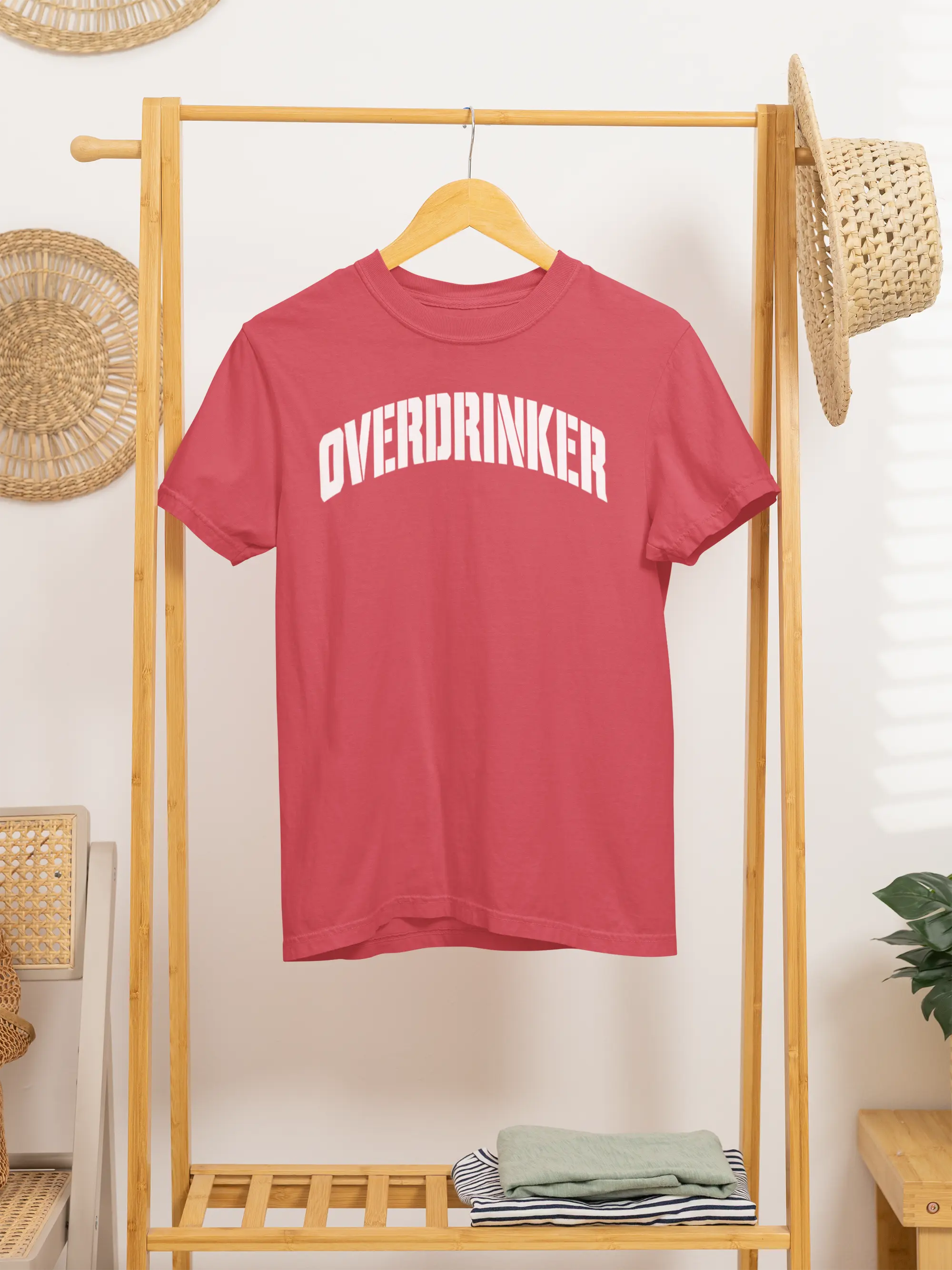 Red t-shirt with 'OVERDRINKER' text on a wooden rack against a white wall.