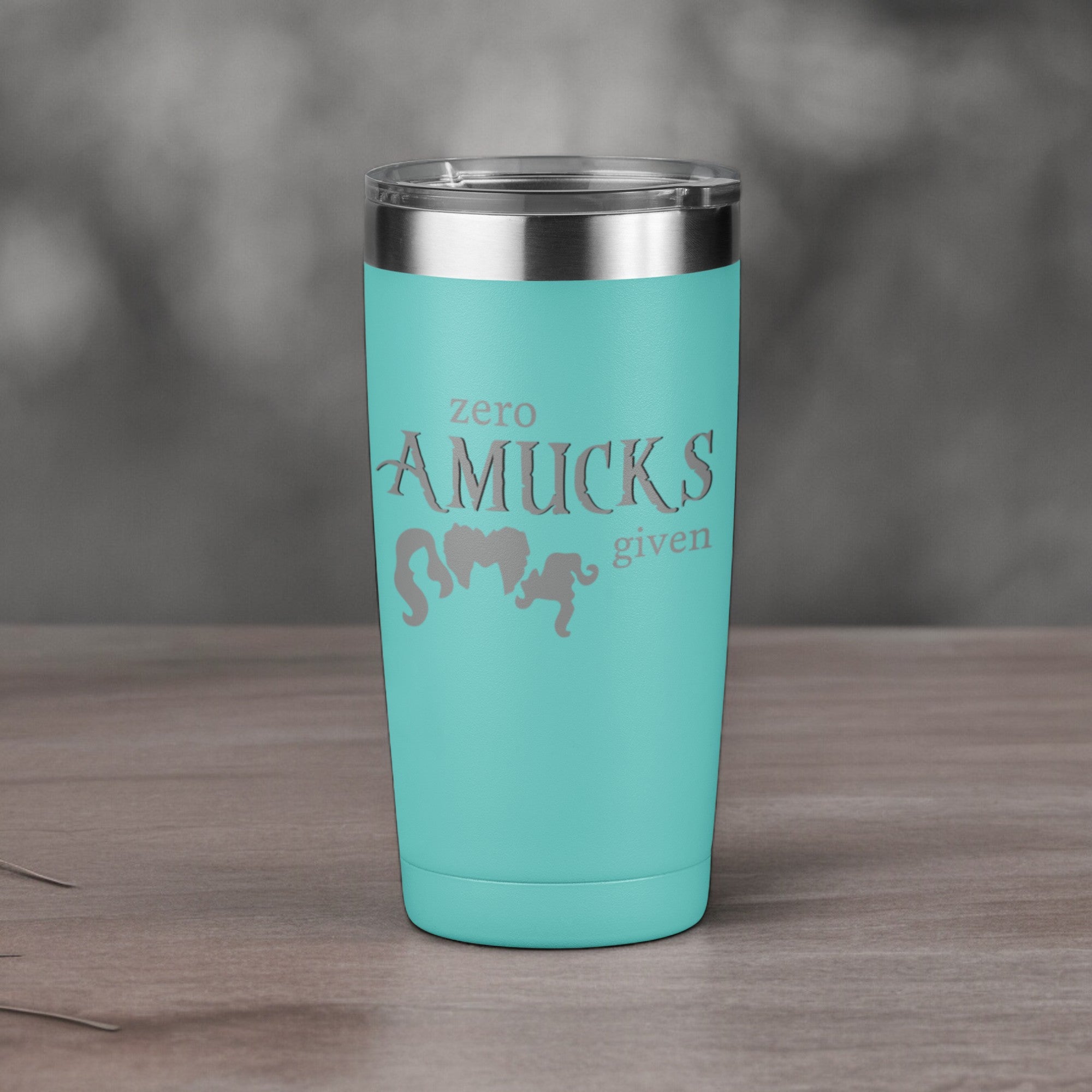 Teal tumbler with silver text that reads "Zero Amucks Given," featuring silhouettes of three witches' hairstyles, perfect for Halloween-themed drinkware.